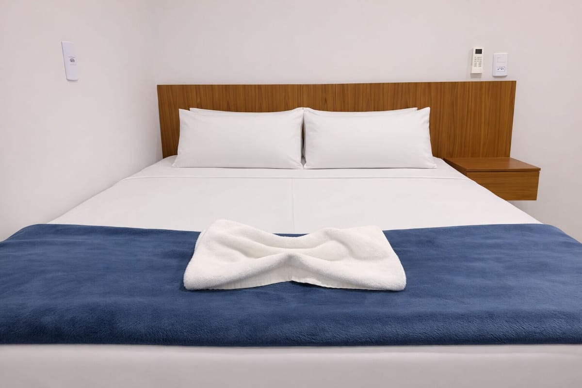 A neatly made bed with white and blue bedding, a wooden headboard, and bedside tables with white lamps.