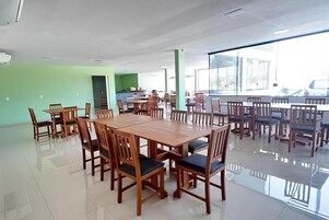 Un comedor amplio con varias mesas y sillas de madera, una pared de acento verde y grandes ventanales que proporcionan luz natural.