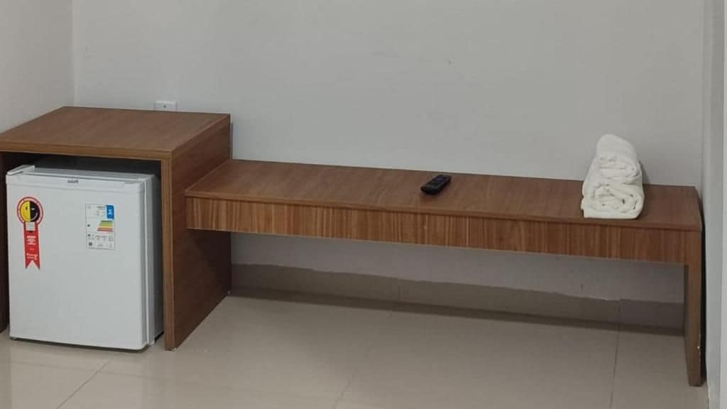 Una habitación con un escritorio de madera, un refrigerador blanco y una toalla doblada sobre el escritorio.