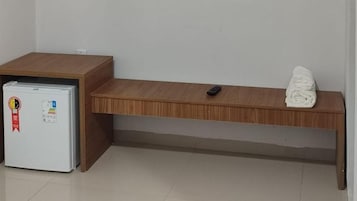 Una habitación con un escritorio de madera, un refrigerador blanco y una toalla doblada sobre el escritorio.