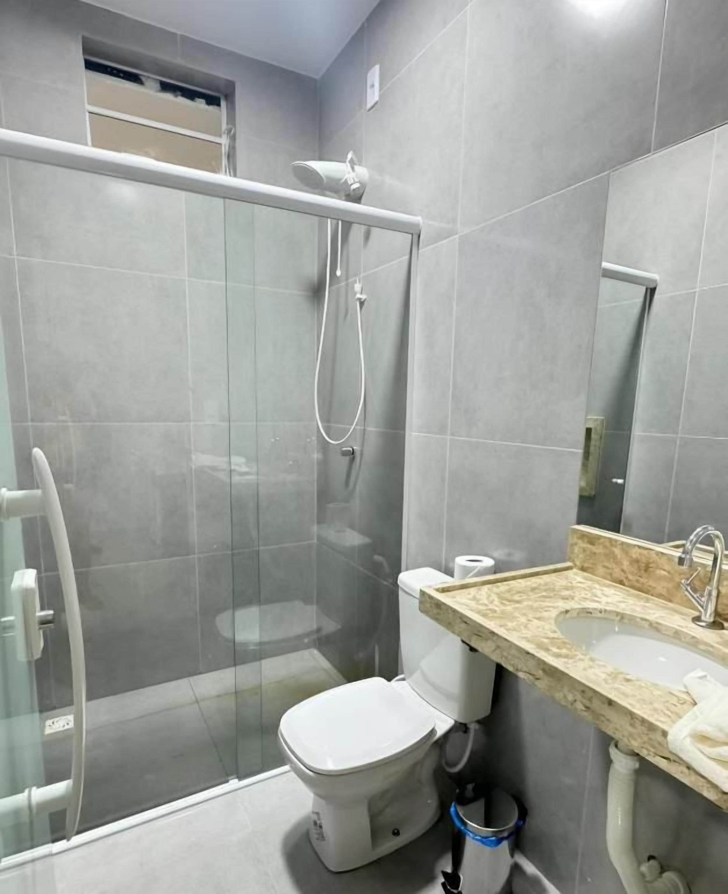 Casa de banho com chuveiro em cabine de vidro, sanita e lavatório com bancada de mármore.
