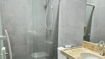 Casa de banho com chuveiro em cabine de vidro, sanita e lavatório com bancada de mármore.