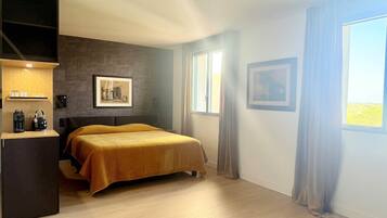 Une chambre à coucher avec un lit, une table de chevet sur laquelle se trouve une bouilloire, une étagère avec des verres et deux tableaux encadrés accrochés au mur.