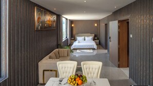 Une chambre d’hôtel avec un lit, une table à manger avec des fruits, un canapé et un tableau au mur.