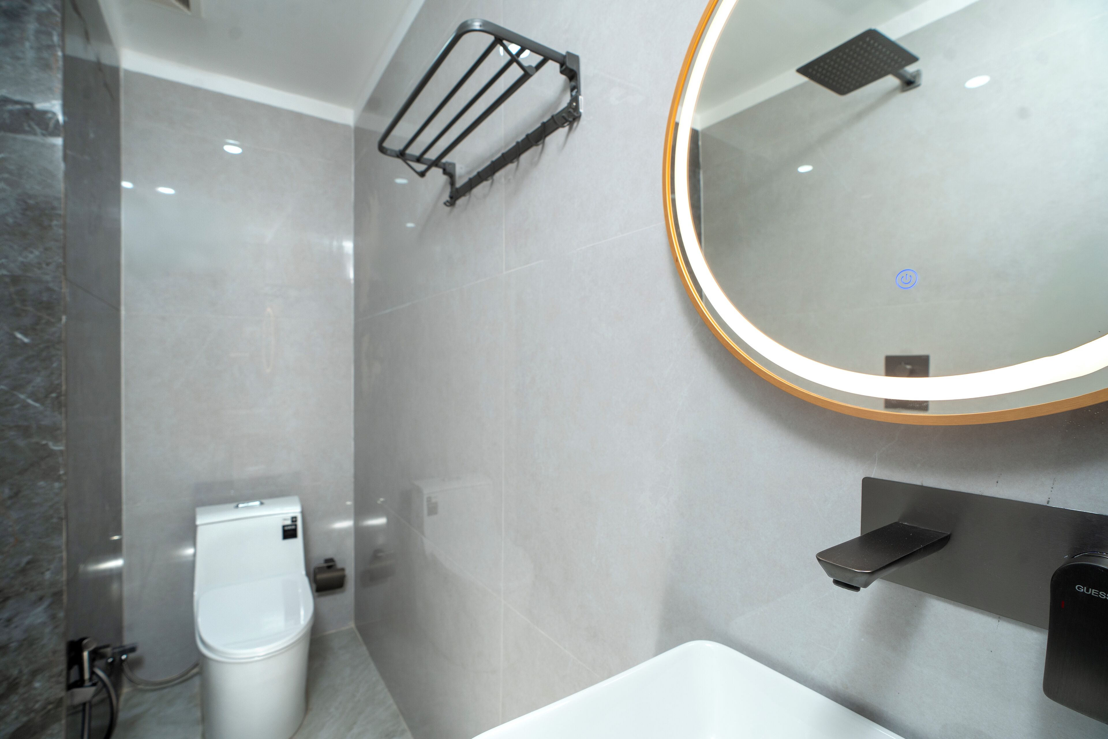 A modern bathroom with a toilet, a sink, a towel rack, and a mirror with a light.