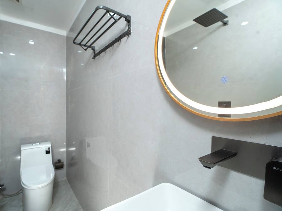 A modern bathroom with a toilet, a sink, a towel rack, and a mirror with a light.