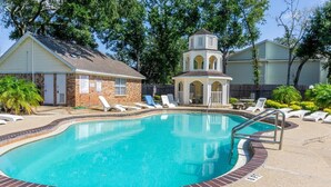A swimming pool with a brick border, a small gazebo, and lounge chairs.