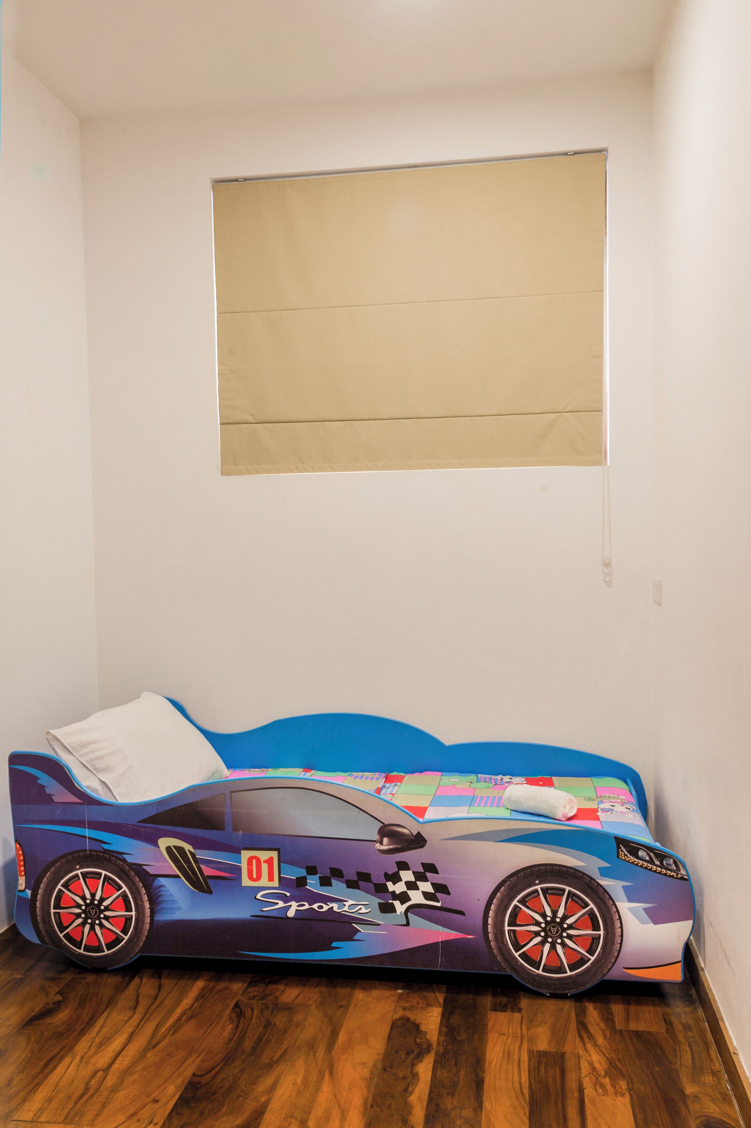 A single bed with a sports car design, a white pillow, and a window with a beige blind.