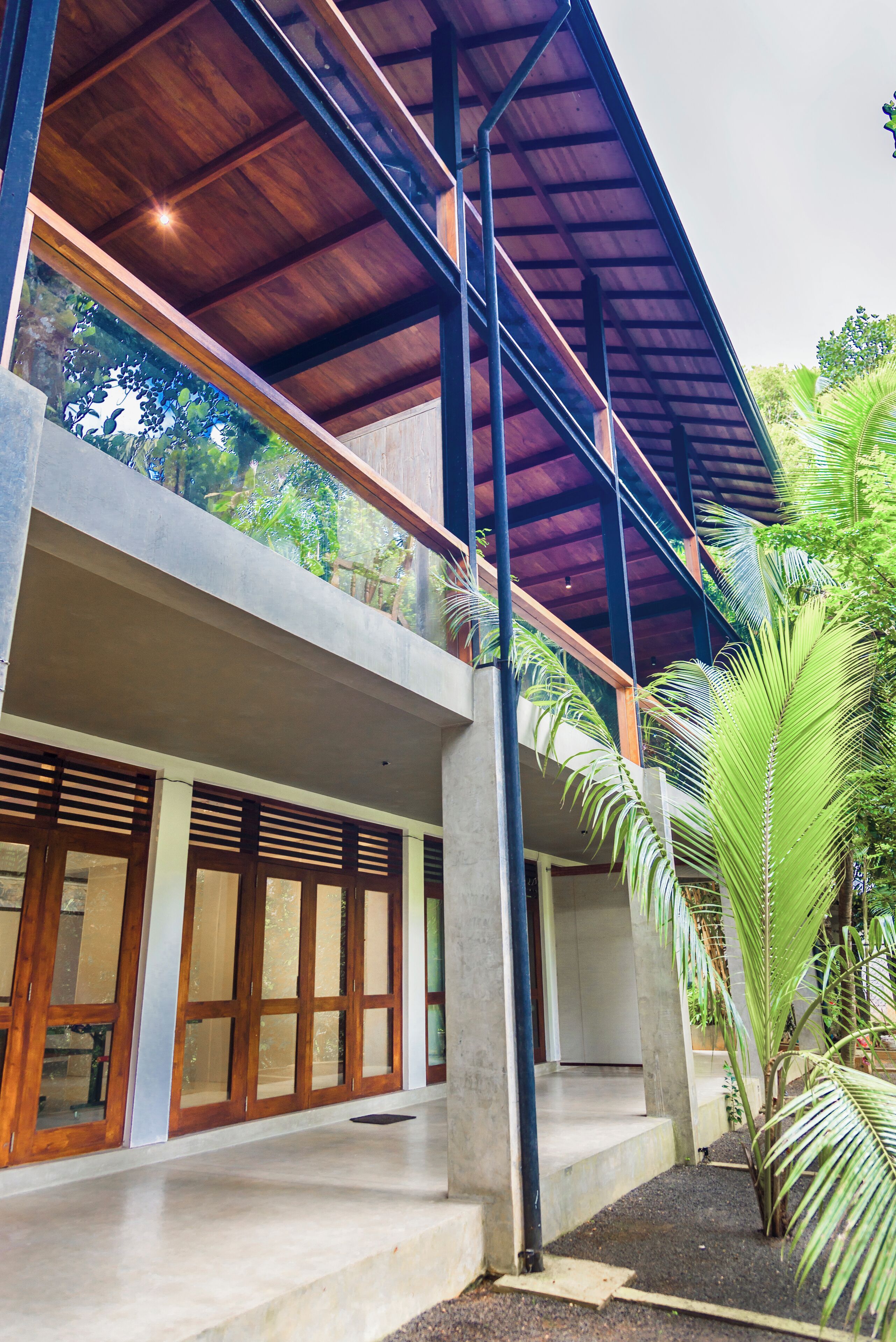 A modern two-story building with a concrete facade, large wooden-framed windows, and a balcony with a wooden roof.