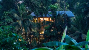 A secluded, tropical-style villa surrounded by dense foliage, featuring a prominent glass facade and a blue roof. - Paradise Itzu (Kobbekaduwa)