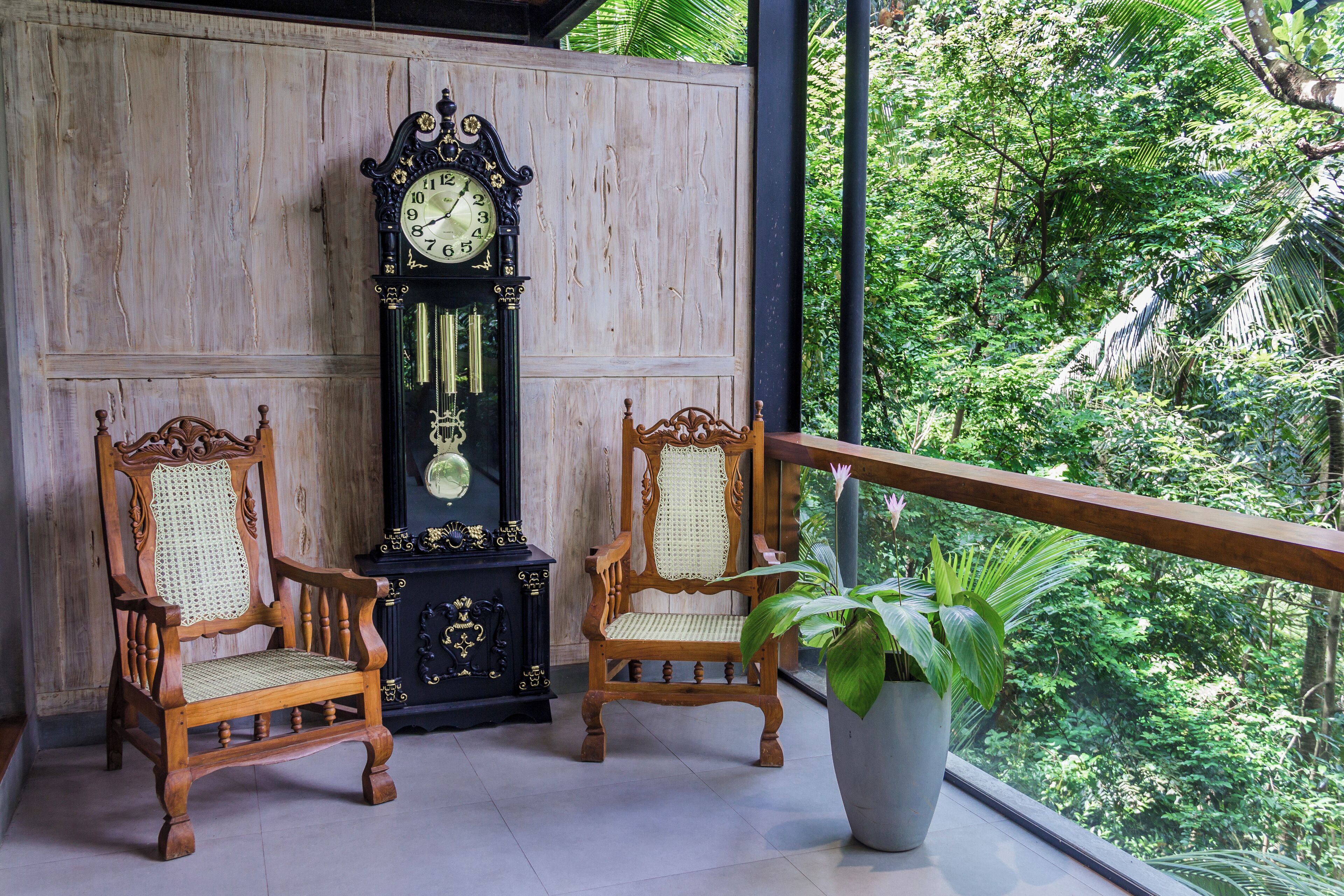 Un balcon avec deux chaises en bois, une grande horloge murale et une plante en pot.