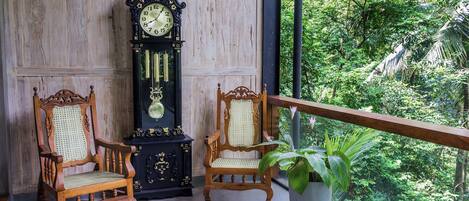 Un balcon avec deux chaises en bois, une grande horloge murale et une plante en pot.