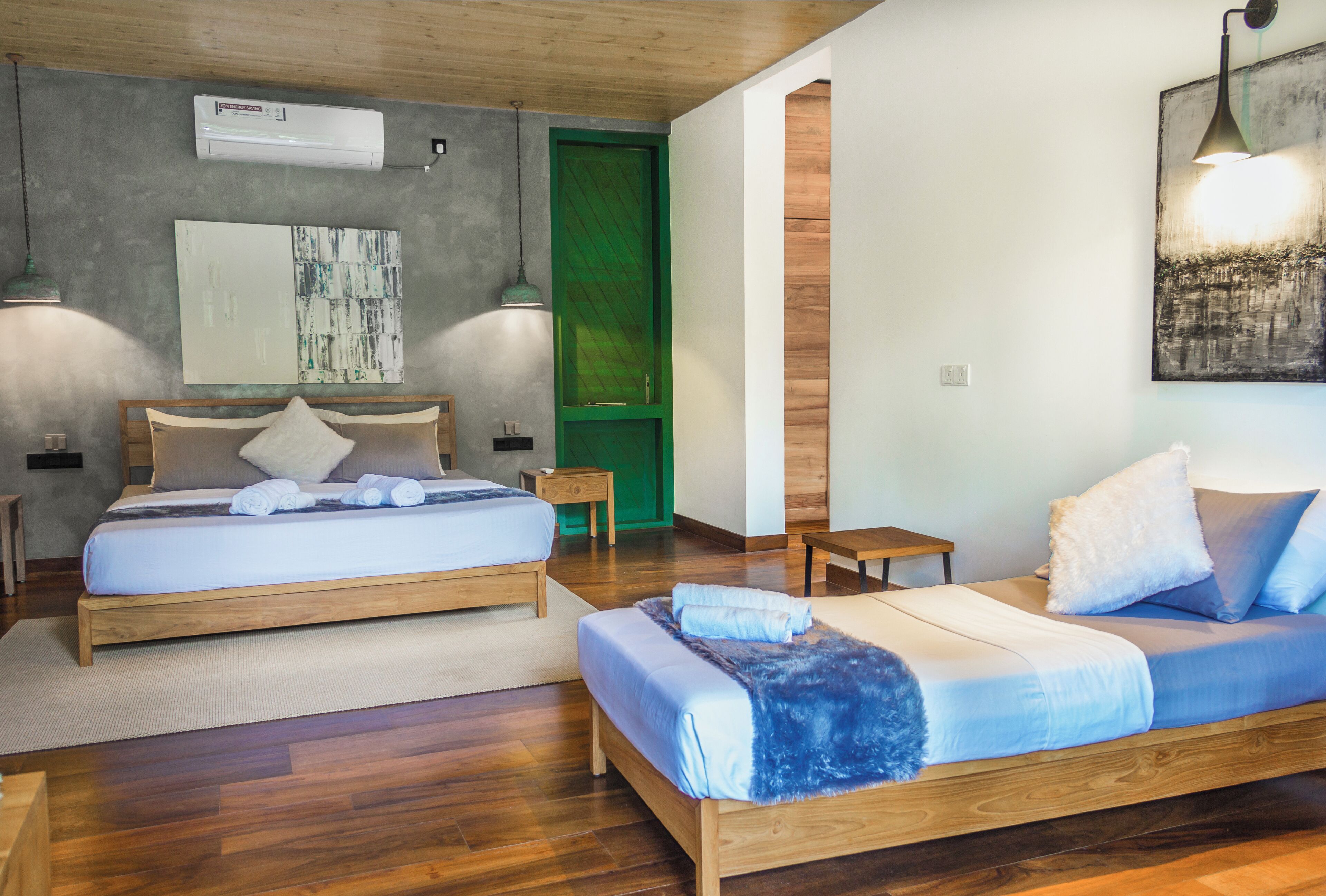 A modern bedroom with two wooden beds, a green door, and artwork on the walls.