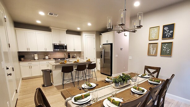Una cocina moderna con armarios blancos, una isla central con taburetes y un comedor con mesa de madera para seis.