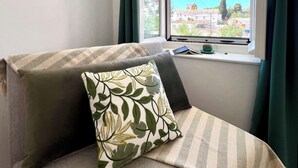 Una habitación con una cama, una ventana con vistas a edificios y montañas, y un equipo de aire acondicionado.