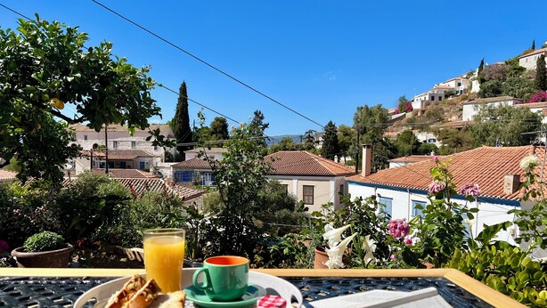 Bandeja de desayuno con croissants, jugo y una taza sobre una mesa con vista a un pueblo en la colina.