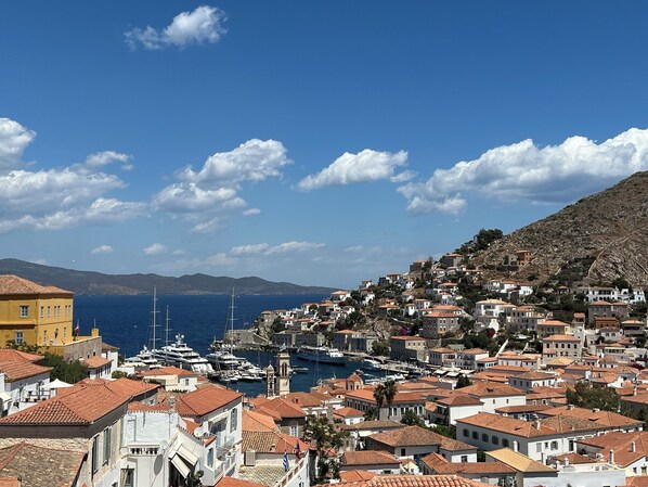 A coastal town with terracotta-roofed buildings, a marina with boats, and a clear blue sky. - Hydra Serene Escape (Idra)