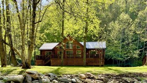 Een houten hut met een terras en een pad van stenen dat naar een beekje leidt.