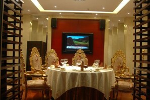 A dining area with a television screen, ornate chairs, and a table set for a meal. - Qilu Wangfu Hotel (Laiyang)