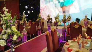 A banquet hall with tables set for a formal event, featuring floral centerpieces and a projection screen in the background.
