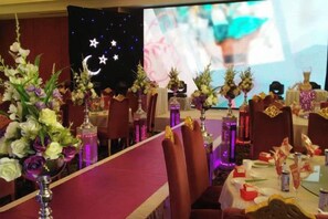 A banquet hall with tables set for a formal event, featuring floral centerpieces and a projection screen in the background. - Qilu Wangfu Hotel (Laiyang)