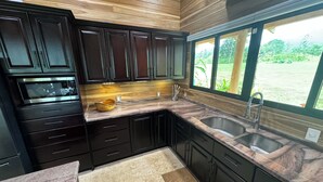 A modern kitchen with dark cabinets, a marble countertop, and a large window offering a view of greenery. - Nestled at the base of Rincon de la Vieja Volcano and bordering the Rio Celeste. (Buenas Aires)