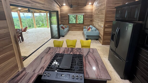 A modern kitchen with a gas stove, a black refrigerator, and a dining area with yellow chairs. - Nestled at the base of Rincon de la Vieja Volcano and bordering the Rio Celeste. (Buenas Aires)