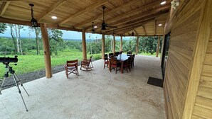 A covered outdoor dining area with a table and chairs, a telescope on a tripod, and a view of a lush landscape. - Nestled at the base of Rincon de la Vieja Volcano and bordering the Rio Celeste. (Buenas Aires)