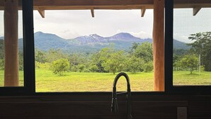 A kitchen with a sink and a view of a mountainous landscape through large windows. - Nestled at the base of Rincon de la Vieja Volcano and bordering the Rio Celeste. (Buenas Aires)