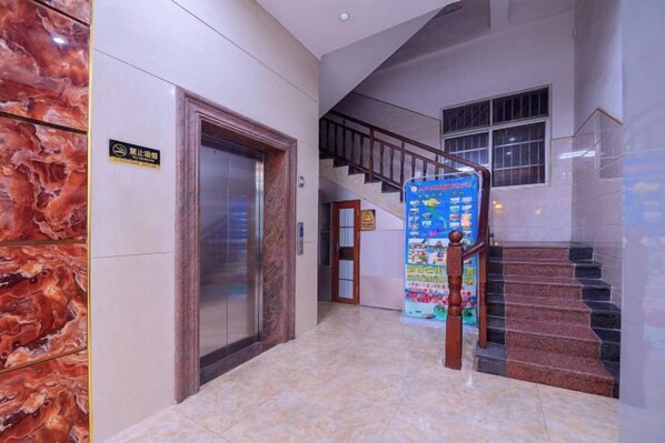 A hotel lobby with a marble floor, an elevator, a staircase, and a signboard.