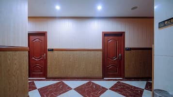 A hotel lobby with two wooden doors, a marble-patterned floor, and a trash can.