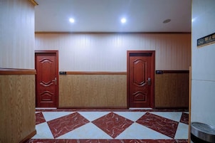 Un vestíbulo de hotel con dos puertas de madera, un suelo con diseño de mármol y un cesto de basura.