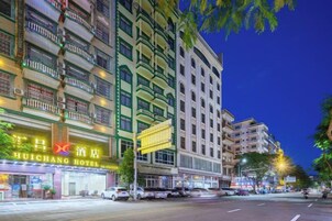 Un hotel de varios pisos, con un cartel llamativo y vista a la calle con coches estacionados.
