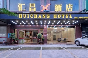 Exterior do Hotel Huichang, com área de recepção, portas de vidro e um espaço de estacionamento visível.