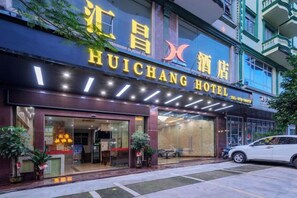 El exterior del Hotel Huichang, con un cartel llamativo, una entrada de vidrio y un coche estacionado en la parte delantera.