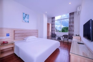 Quarto de hotel com cama, escrivaninha, cadeira, televisão e janela com vista.