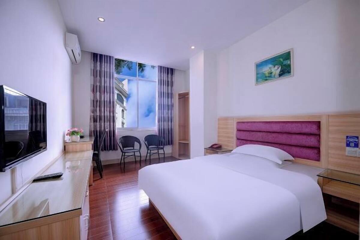 Ein Hotelzimmer mit Bett, Fernseher, Schreibtisch, Stuhl und einem Fenster mit Vorhängen.