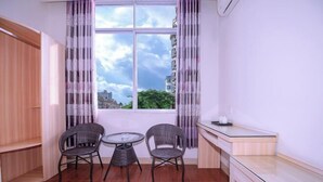 A room with a window, two wicker chairs, a small round table, a wooden desk, and a white wall. - Dongxing Huichang Fashion Hotel (Dongxing)
