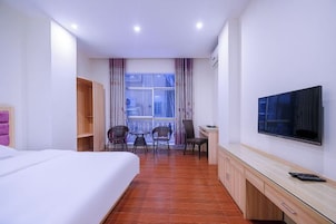 Quarto de hotel com cama, escrivaninha com televisão, mesa pequena com cadeiras e janela com cortinas.