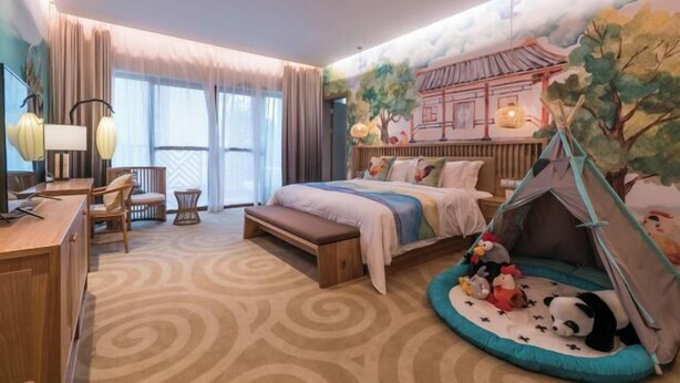 A hotel room with a bed, a desk, a chair, a bench, a tent, and a mural of a traditional building. - Dongxing Huichang Fashion Hotel (Dongxing)