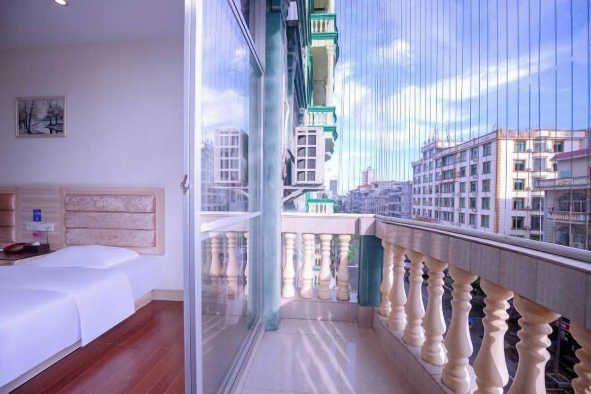 Ein Schlafzimmer mit Bett, Nachttisch und Fenster mit Blick auf Gebäude.