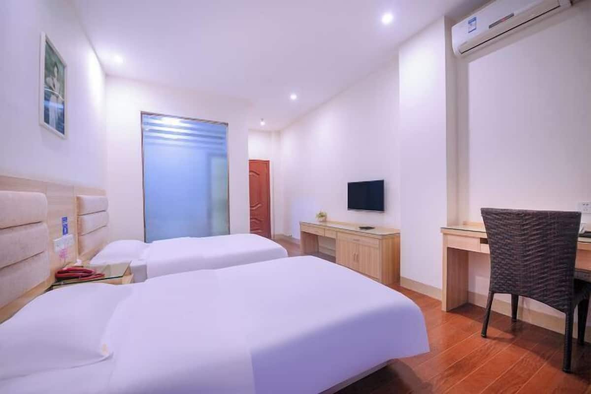 Ein Hotelzimmer mit zwei Betten, einem Schreibtisch, einem Sessel, einem Fernseher und einer Klimaanlage.