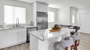 A modern kitchen with white cabinetry, a marble island, and bar stools.