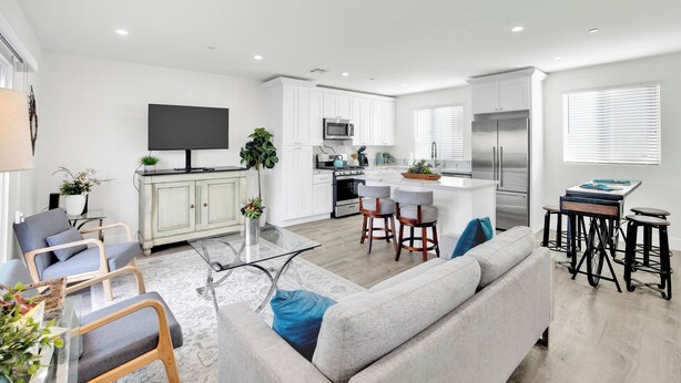 A modern kitchen with white cabinets, a stainless steel refrigerator, and a flat-screen TV mounted above the counter.