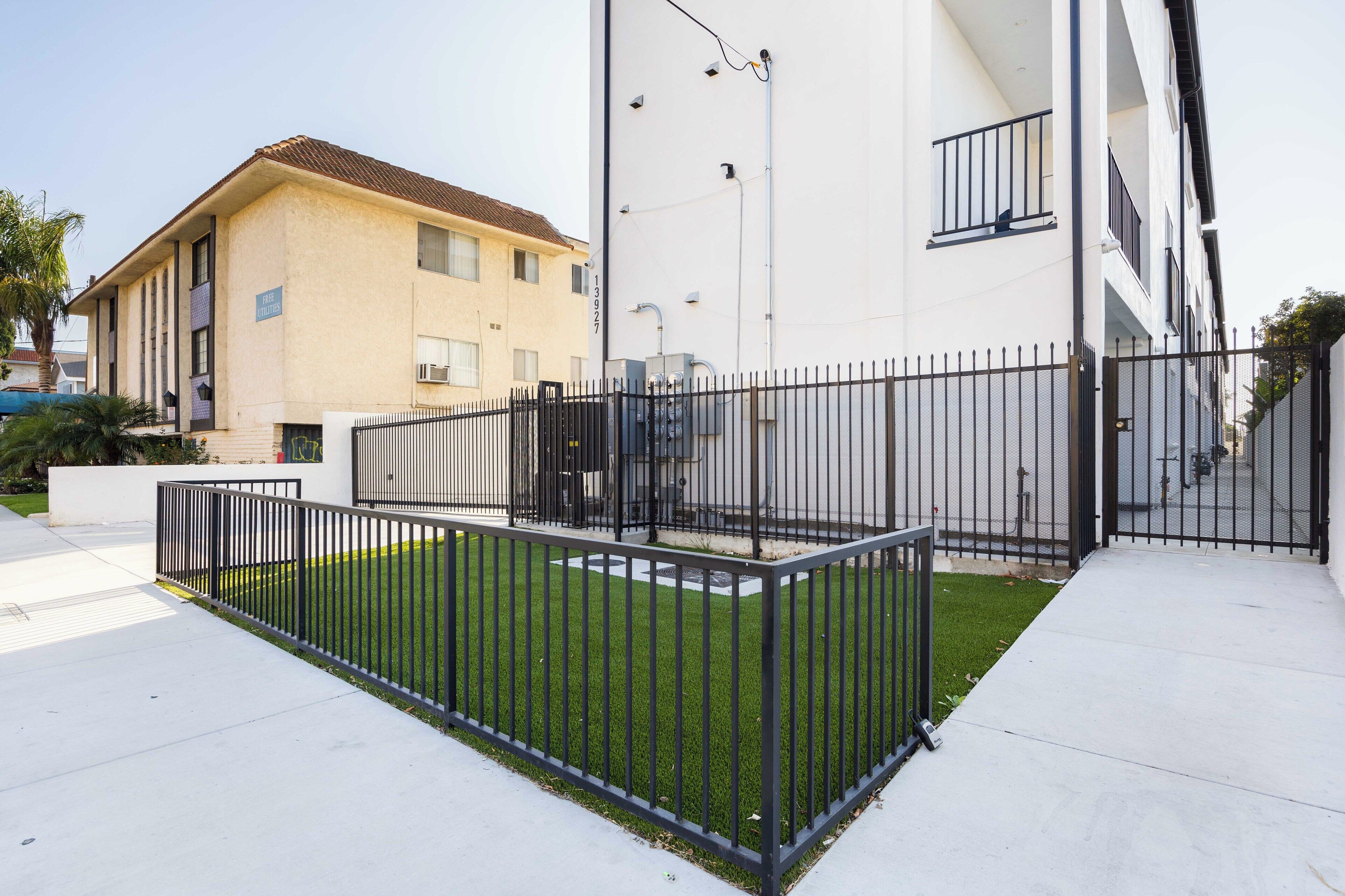 Un bâtiment moderne doté d’une entrée sécurisée par un portail, d’une pelouse bien entretenue et surplombant un ciel dégagé.