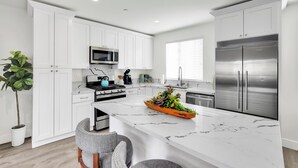 A modern kitchen with white cabinetry, a marble countertop, stainless steel appliances, and a central island with a plant arrangement.
