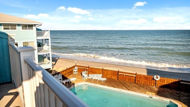A pool area with a wooden deck, lounge chairs, and a view of the ocean. - Shorething- oceanfront-pool View-third floor condo -sleeps 6 (Kure Beach)