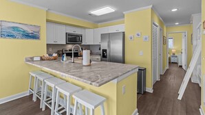 A modern kitchen with white cabinets, stainless steel appliances, and a marble island with bar stools. - Shorething- oceanfront-pool View-third floor condo -sleeps 6 (Kure Beach)