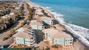 A beachfront hotel with multiple-story buildings, a parking lot, and a road running parallel to the beach. - Shorething- oceanfront-pool View-third floor condo -sleeps 6 (Kure Beach)