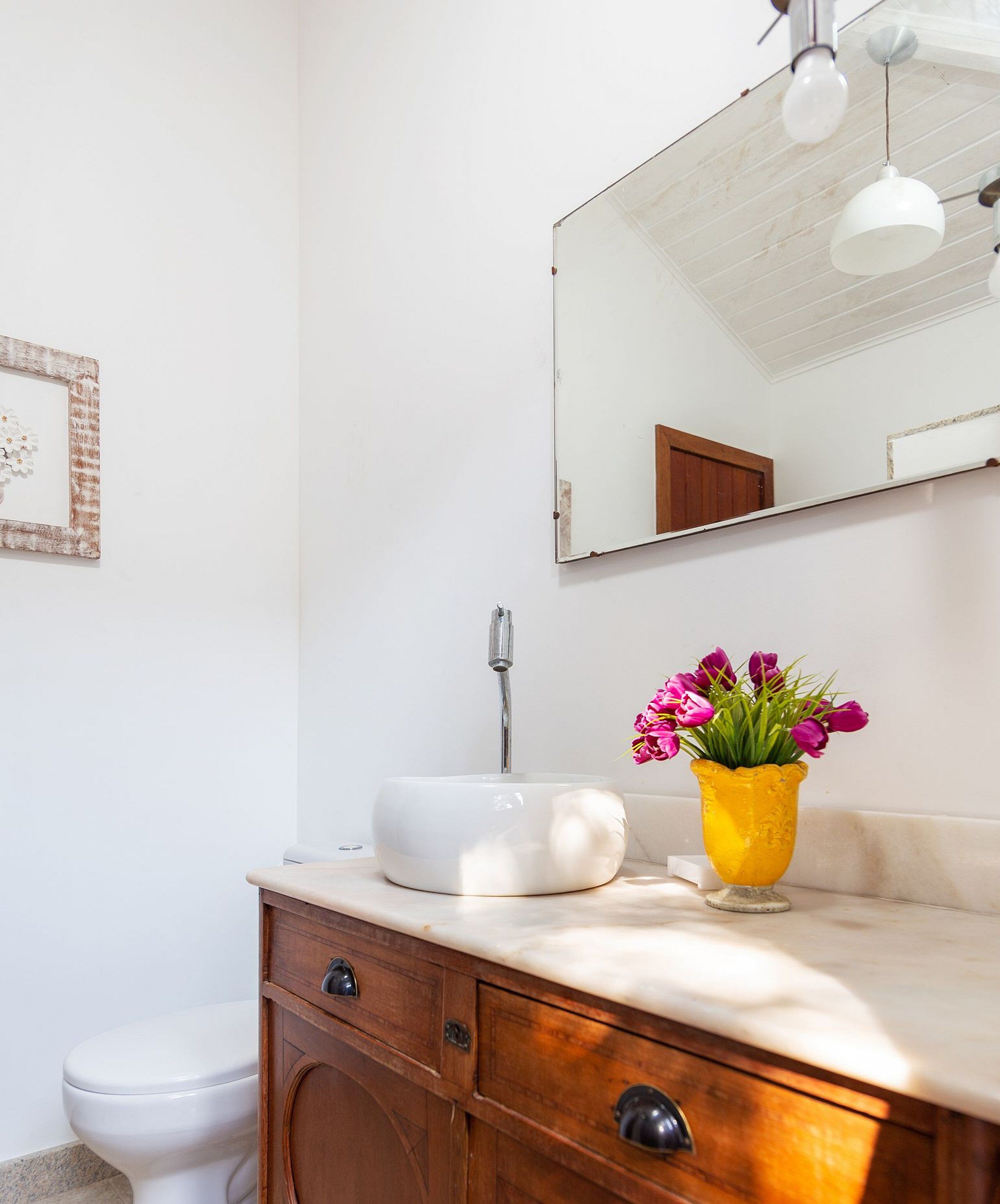 Ein Badezimmer mit einem weißen Waschbecken, einem Holzkorpus und einer gelben Vase mit Blumen.